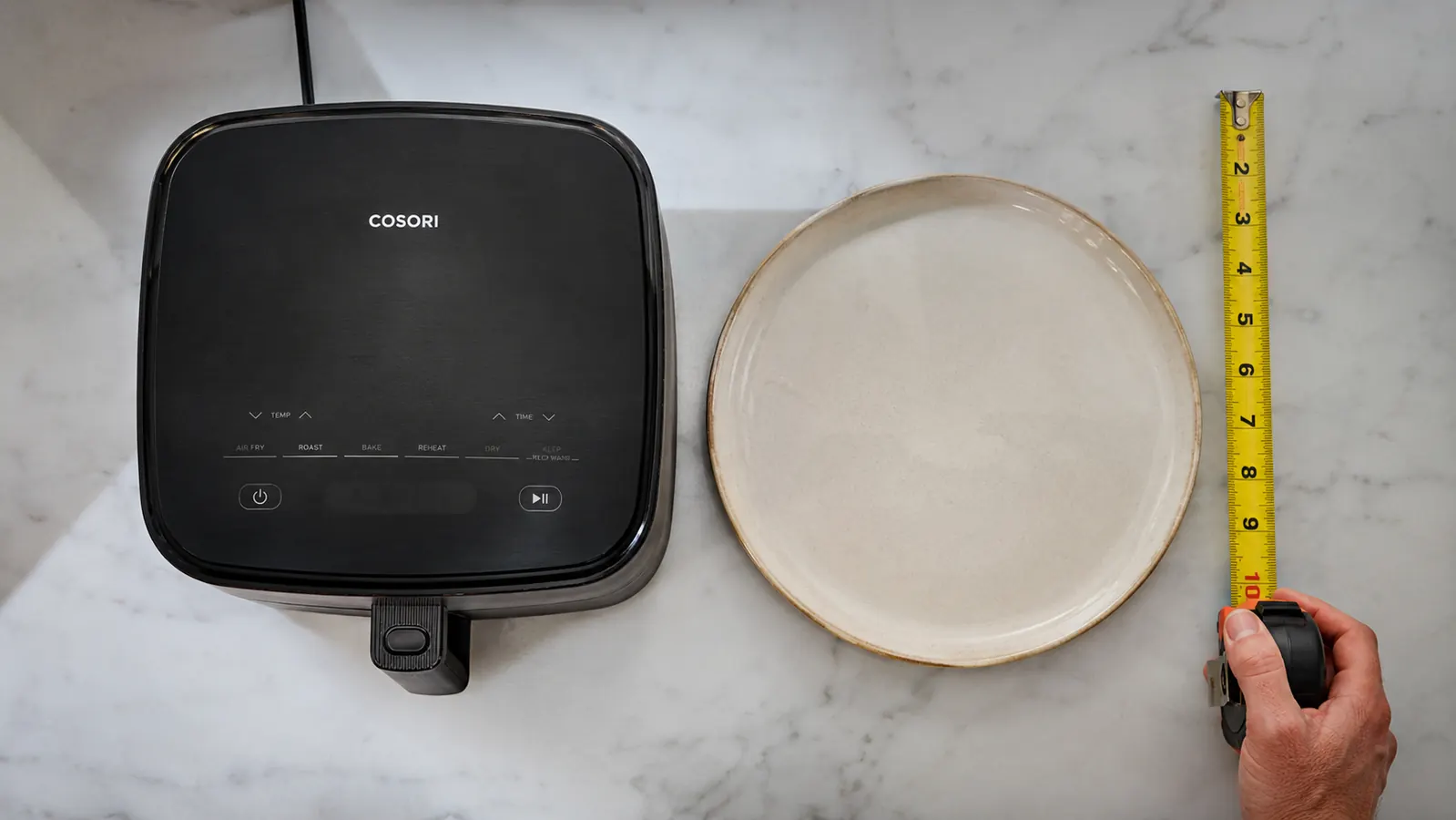 Top-down measurement comparison showing the Ninja AF101 footprint against a standard 12-inch dinner plate on a counter