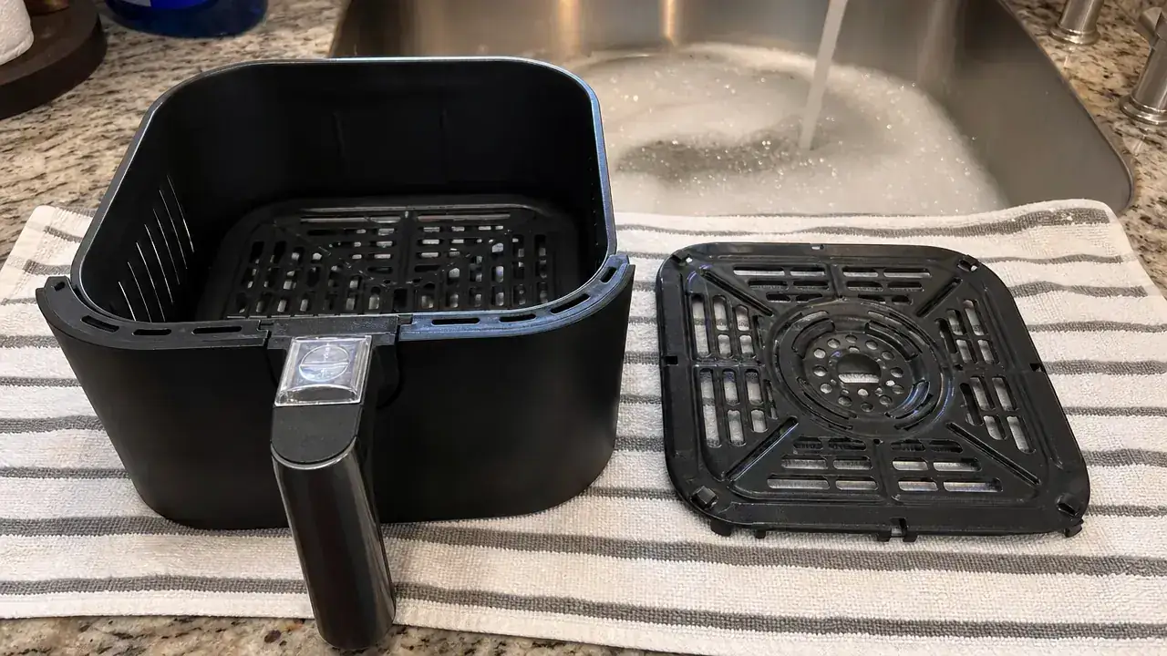 Ninja AF101 basket and crisper plate separated and laid out next to a kitchen sink ready for hand washing