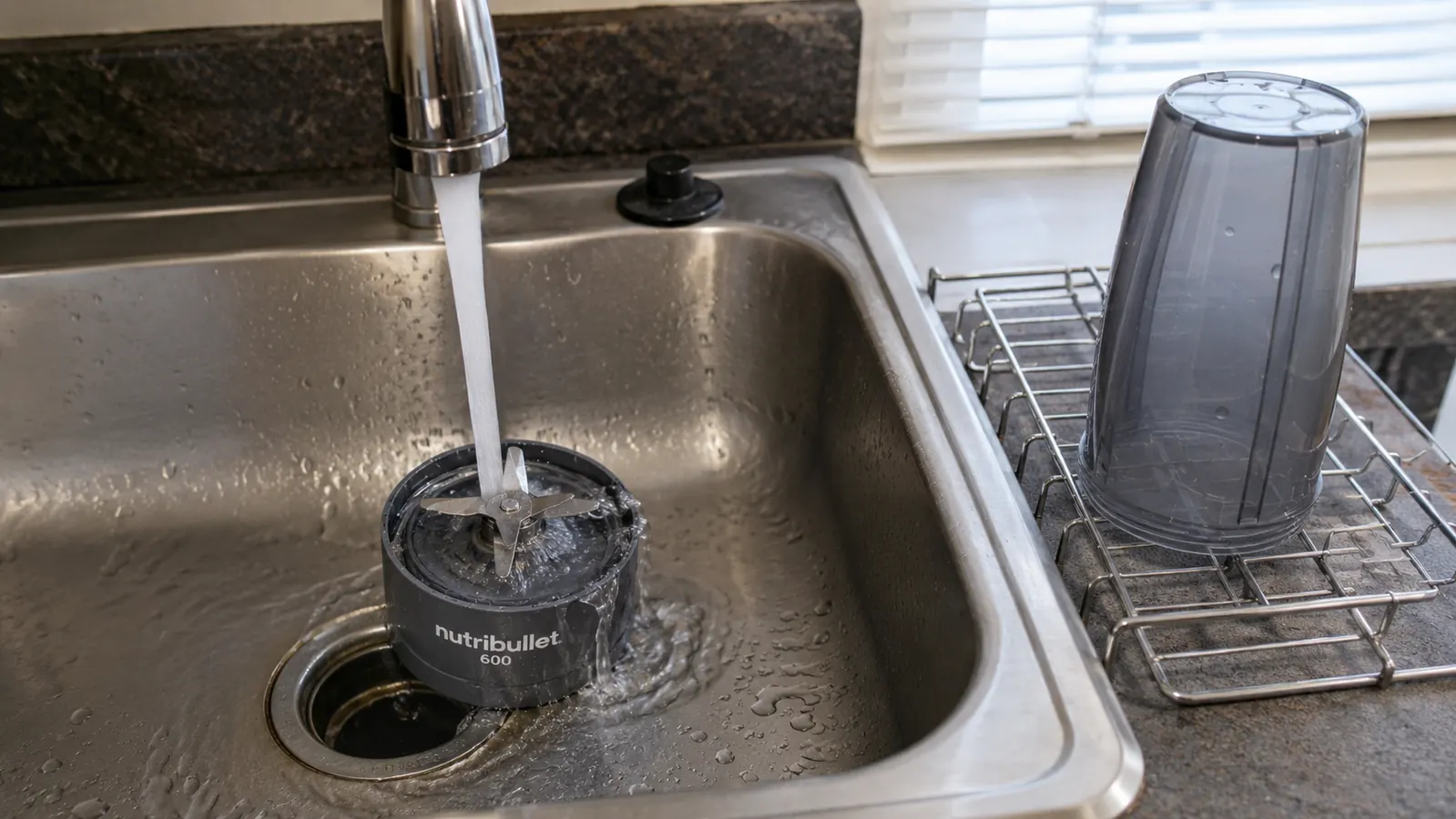 NutriBullet 600 cup and blade assembly next to a kitchen sink, showing cleaning with a brush